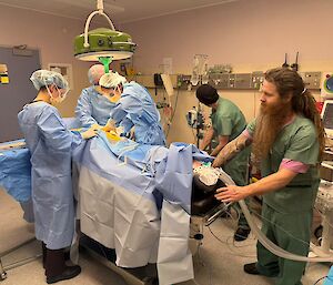 Five people wearing medical scrubs gather around a dummy laying on an operating table