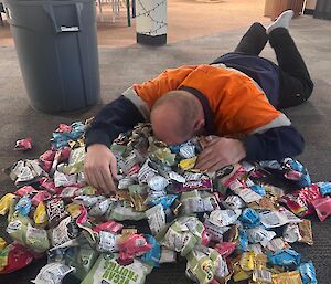 A man lies on the floor next to a massive pile of snacks