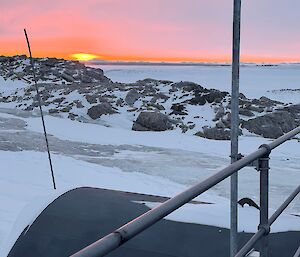 The sun rising over snow and grey rock
