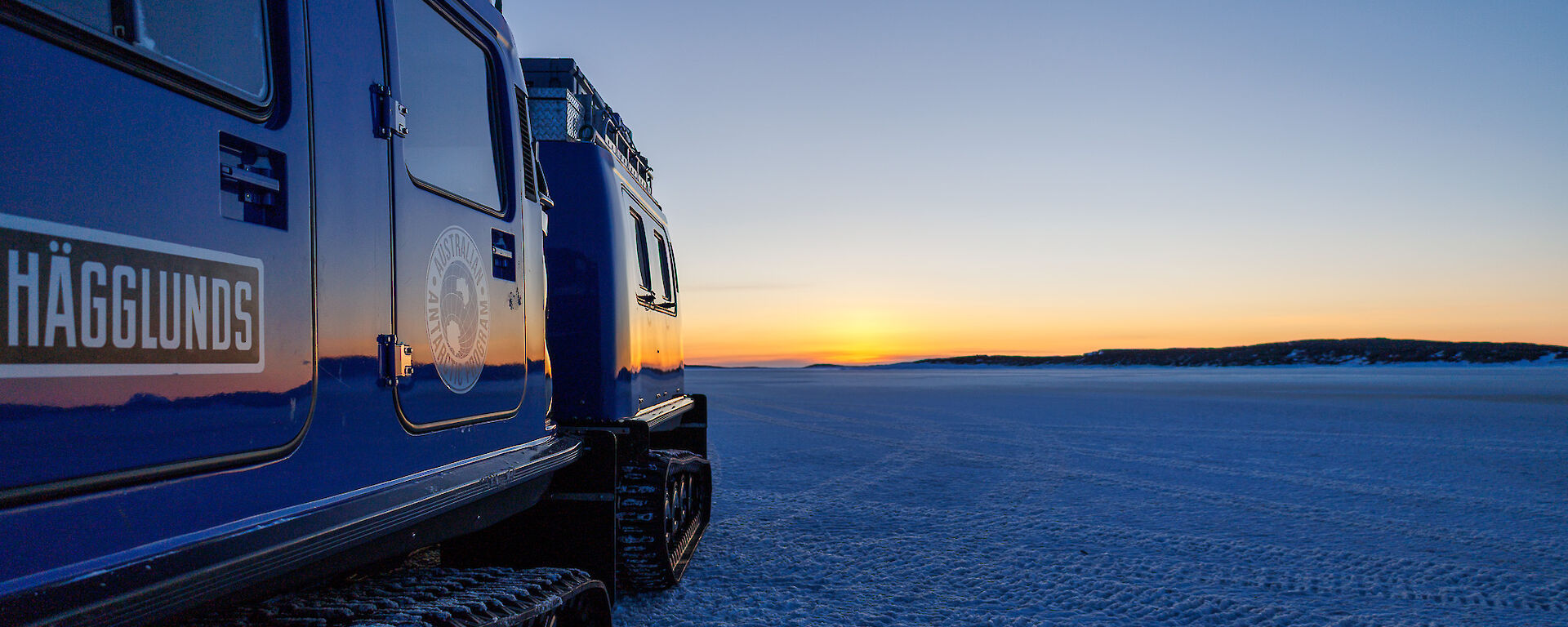A sunset over the sea ice reflects off the side of a Hagglund