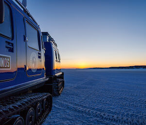 A sunset over the sea ice reflects off the side of a Hagglund