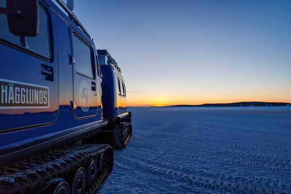A sunset over the sea ice reflects off the side of a Hagglund
