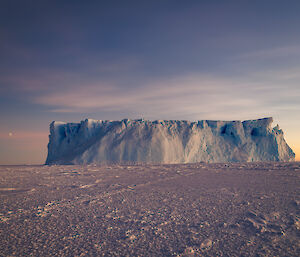 An iceberg features in the sea ice, with clear skies behind it