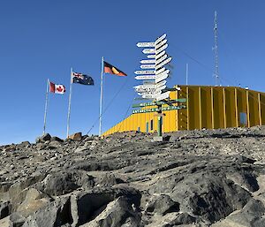 A yellow building is visble in the background under a bold blue sky. In the foreground the Australian, Australian Aboriginal and Canadian flags are streaming in the wind