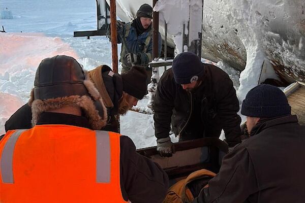 A group in hi vis kneel in the snow around a fuel pump