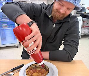 A man puts tomato sauce on a Fray Bentos pie