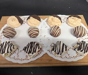 An assortment of petit fours displayed on a wooden serving board, including chocolate-dipped meringues, chocolate truffles drizzled with white chocolate and white chocolate rocky road squares finished with dark chocolate.