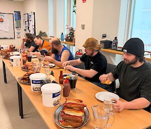 Five expeditioners sitting at a table ready to eat hot dogs