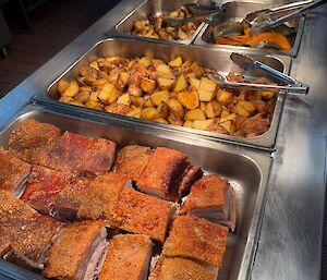 Pork-belly roast keeping warm in the bain marie before being served, including roast vegetables and asparagus