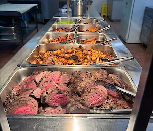 Red meat roast heating in the bain marie before being served, including roast vegetables and peas