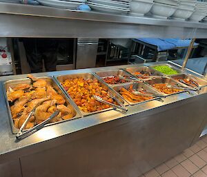 Chicken roast keeping warm in the bain marie before being served, including roast vegetables and peas