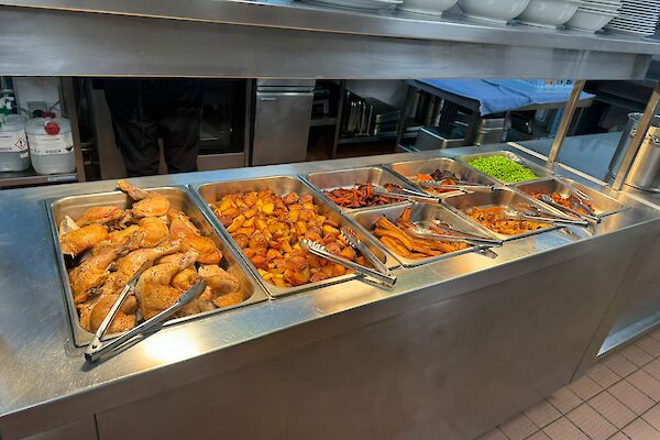 Chicken roast keeping warm in the bain marie before being served, including roast vegetables and peas