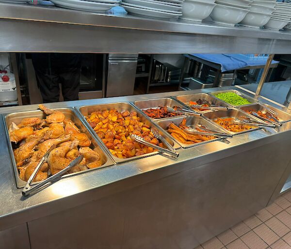Chicken roast keeping warm in the bain marie before being served, including roast vegetables and peas