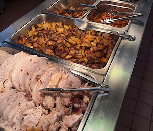 Pork roast keeping warm in the bain marie before being served, including roast vegetables and peas