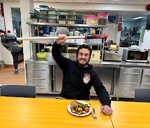 An expeditioner (plumber) at the table with a plate of roast dinner while also holding a Milwaukee stick pump