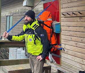 An expeditioner outside a hut at Macquarie Island, wearing a pack that has a large solar panel mounted on it.