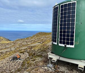 A water-tank with solar panels mounted on it, overlooking a sea view at Macquarie Island
