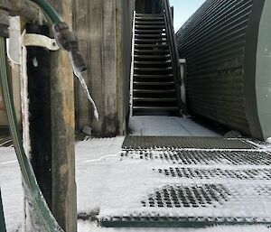The deck and stairs leading to the station cinema are covered by snow. Icicles have formed on the hose and tap nearby.
