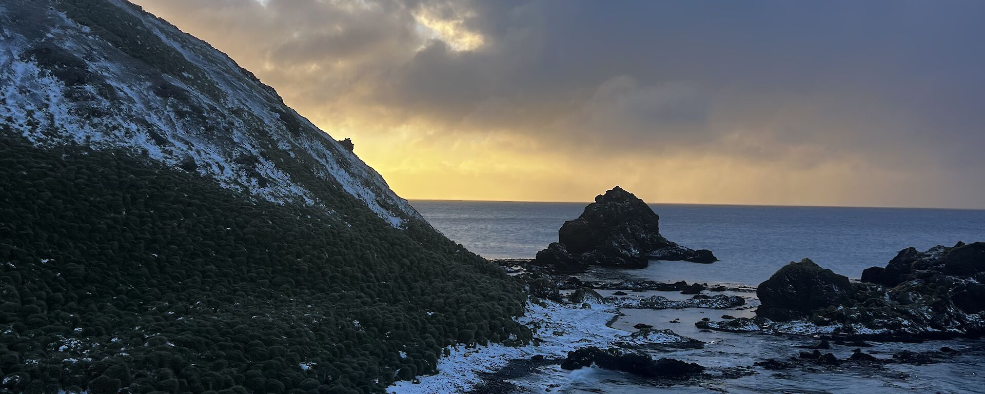 view of the northeast  of Macquarie Island, known as Garden Cove. The sea meets the rocky shoreline which is lightly covered by snow.