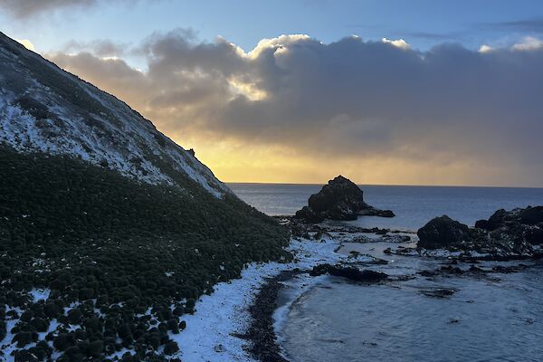 view of the northeast of Macquarie Island, known as Garden Cove. The sea meets the rocky shoreline which is lightly covered by snow.