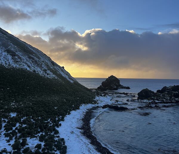 view of the northeast  of Macquarie Island, known as Garden Cove. The sea meets the rocky shoreline which is lightly covered by snow.