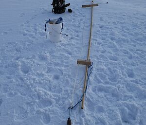 A bamboo pole lays on the sea ice, with a white cable running alongside it, containing the sensor, ready to be installed in the ice