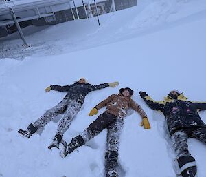 3 female Antarctic expeditioners lying in the fluffy snow making snow angels.