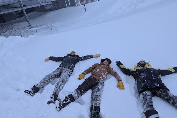 3 female Antarctic expeditioners lying in the fluffy snow making snow angels.