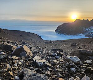 Rocky outcrop falling away to an icy background, with jagged mountain features and rising sun in the background