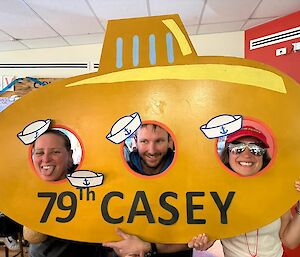 Three people sticking their heads through holes in a sign saying '79th Casey'