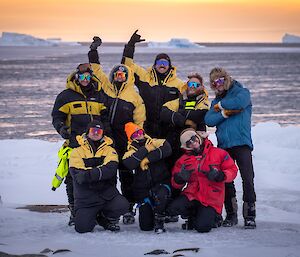 A group of people posing for the camera standing on ice with water behind