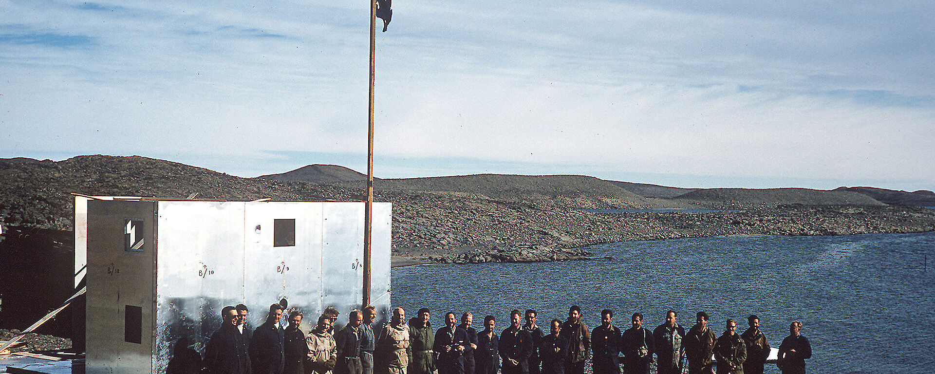 A group of people standing next to a flagpole flying the Australian National Flag and a partially built building
