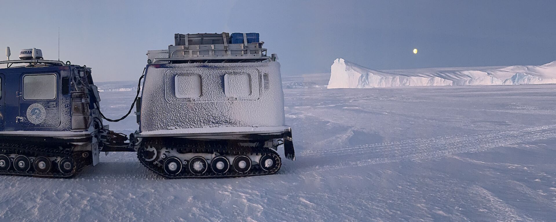 A Hagglands vehicle on the sea ice early morning, overlooking ice cliffs in the background with a bright moon above