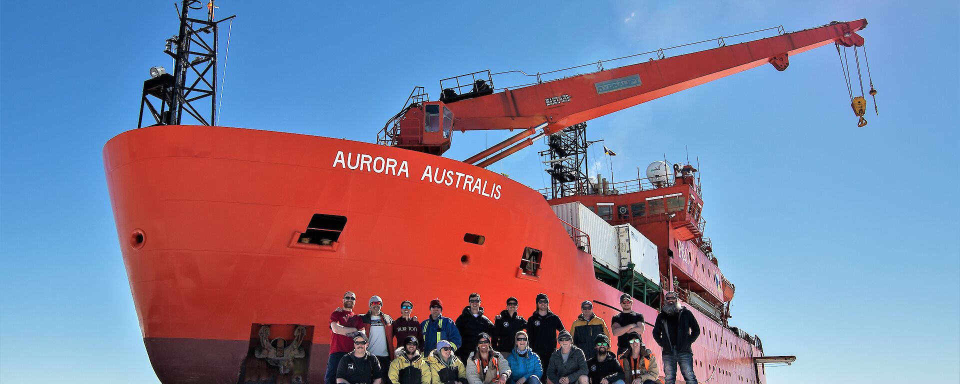 A group standing on ice next to a big red ship