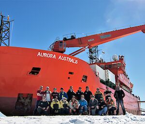 A group standing on ice next to a big red ship