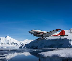 A red and white passenger plane flying over water ice and snow covered mountains