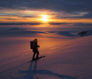 A person skiing across a snowy slope in the sunset