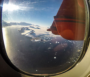 Looking out a plane window to an icy landscape and sea