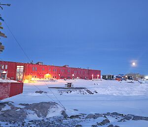 A red corrugated iron shed with the lights on, snow all around and a sign post in the foreground