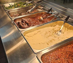 A stainless steel bain marie with vegetables, meat and mashed potato