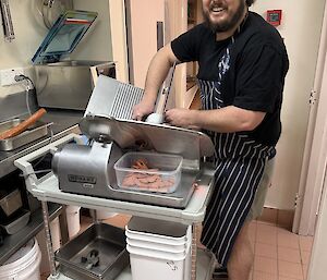 An expeditioner in the kitchen, slicing pepperoni with a large meat-slicing machine