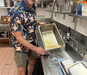 An expeditioner in a loud shirt, washing dishes in the kitchen