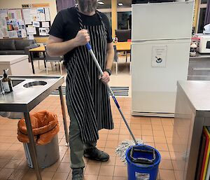 An expeditioner in the kitchen, holding a mop and cleaning the floors