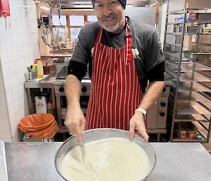 An expeditioner in the kitchen, whisking batter in a large aluminium bowl