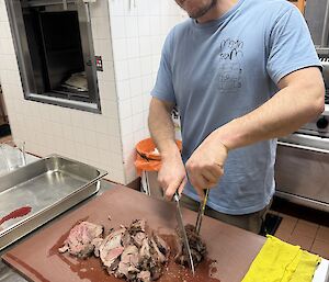 An expeditioner in the kitchen, cutting roast lamb on a cutting board