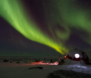 A green aurora stretches into the sky above an apple hut with light visible in the windows