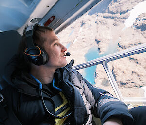 A man wearing a headset looks out of a helicopter window with a smile on his face