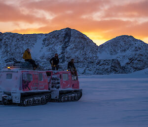 Three expeditioners sit atop a pink Hagglund's vehicle with a golden sunset