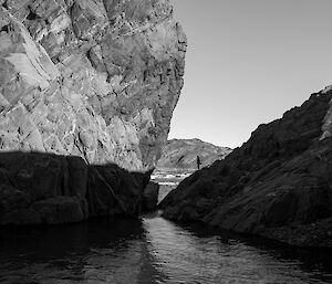 The silhouette of an expeditioner stands between two parge rocks next to a lake