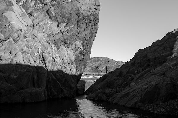 The silhouette of an expeditioner stands between two parge rocks next to a lake